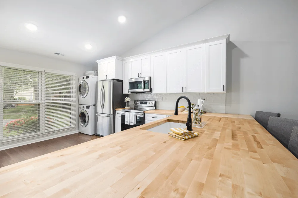 A very clean kitchen, with wood grain design countertops, modern in-kitchen washer and dryer, and modern stainless-steel kitchen appliances.